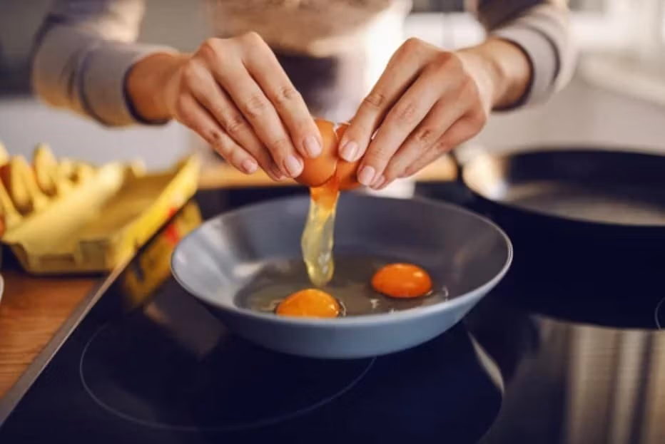 Support worker cracking eggs into a frying pan during meal preparation