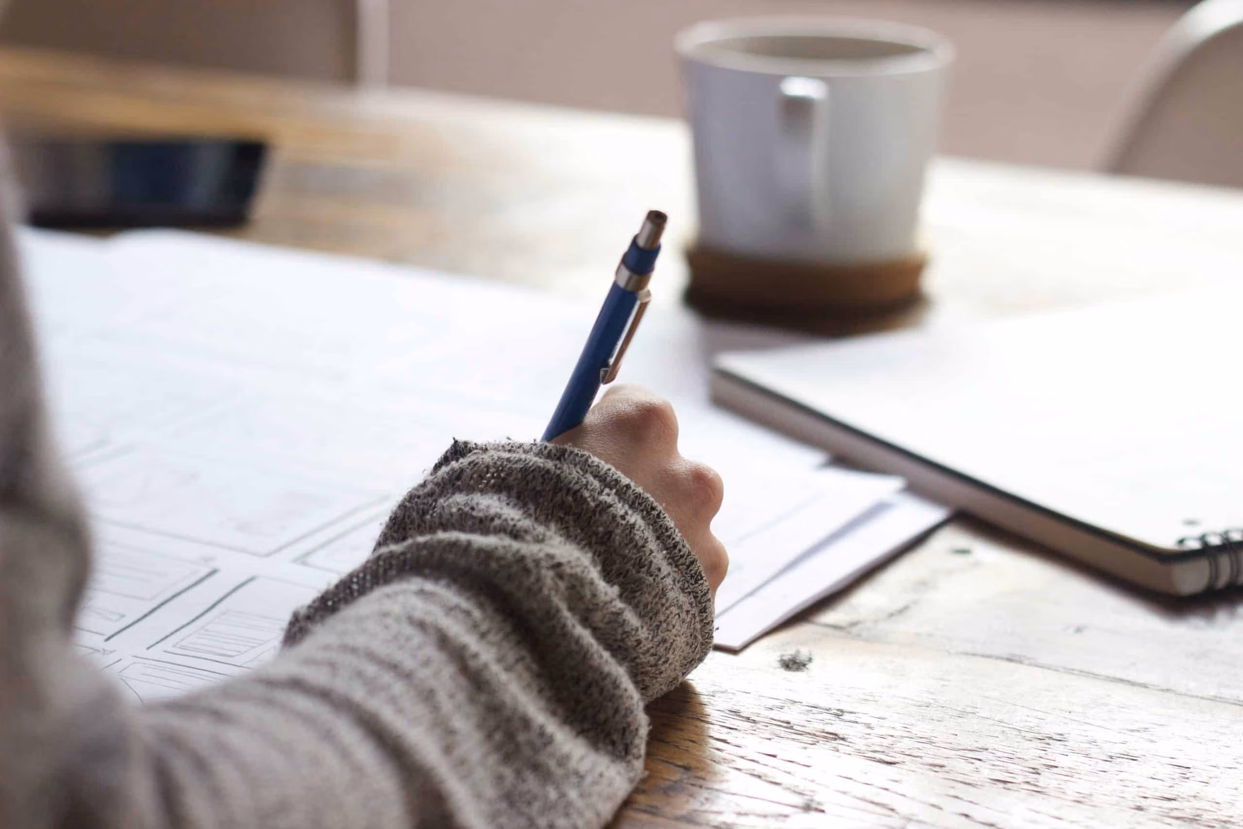 Person filling out paperwork at a desk with a pen and a cup of coffee nearby