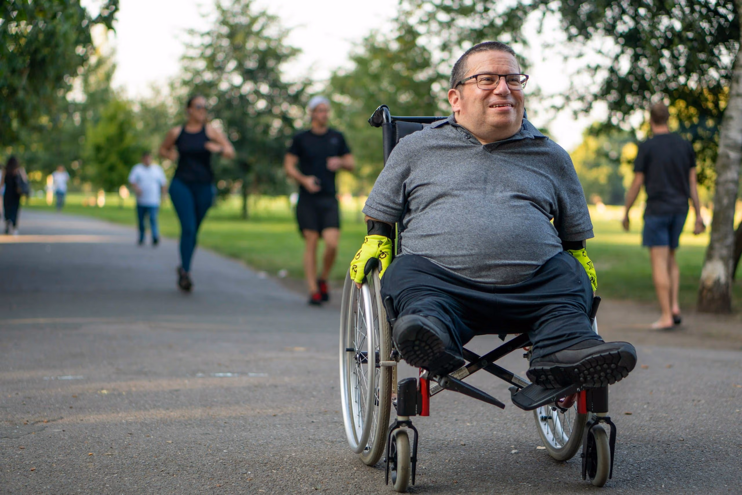 Participant in a wheelchair enjoying time outdoors at a public park on a shared path.