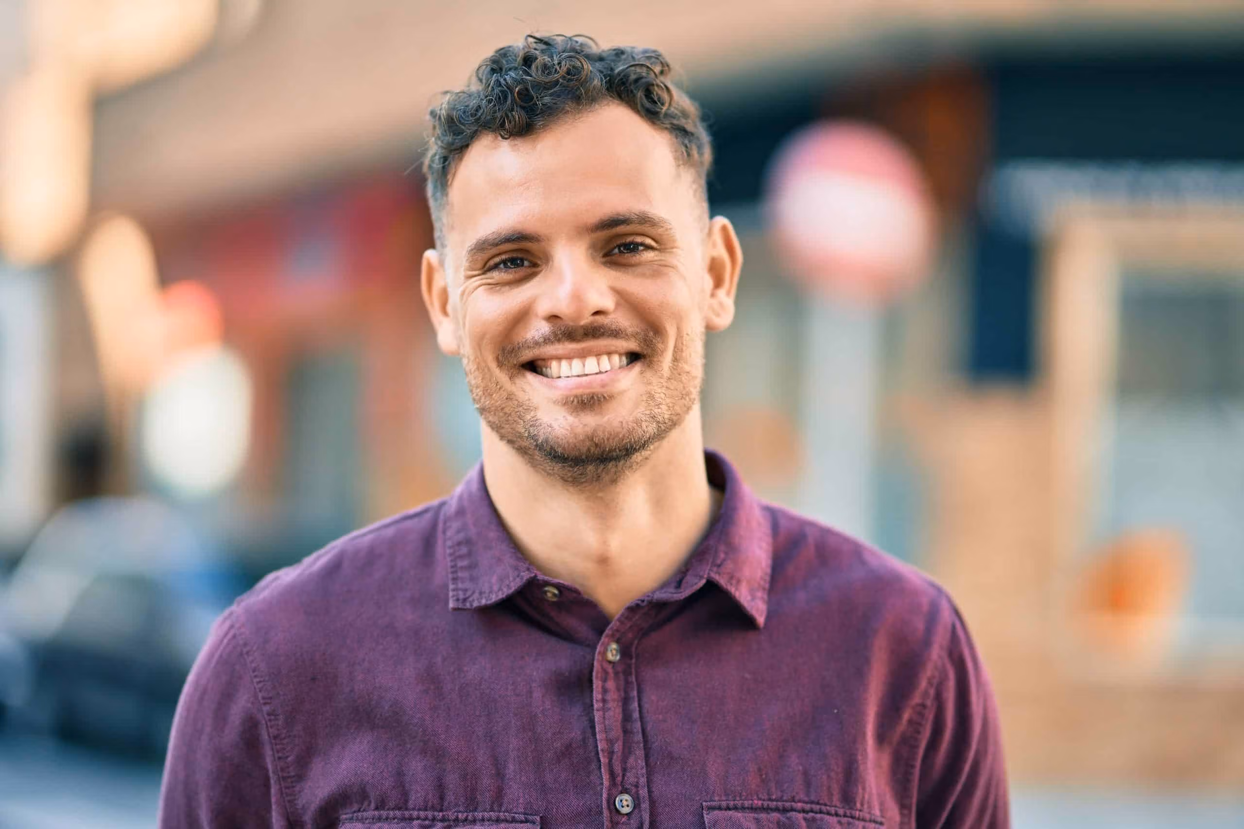 Male support worker smiling while standing outdoors in a community area.