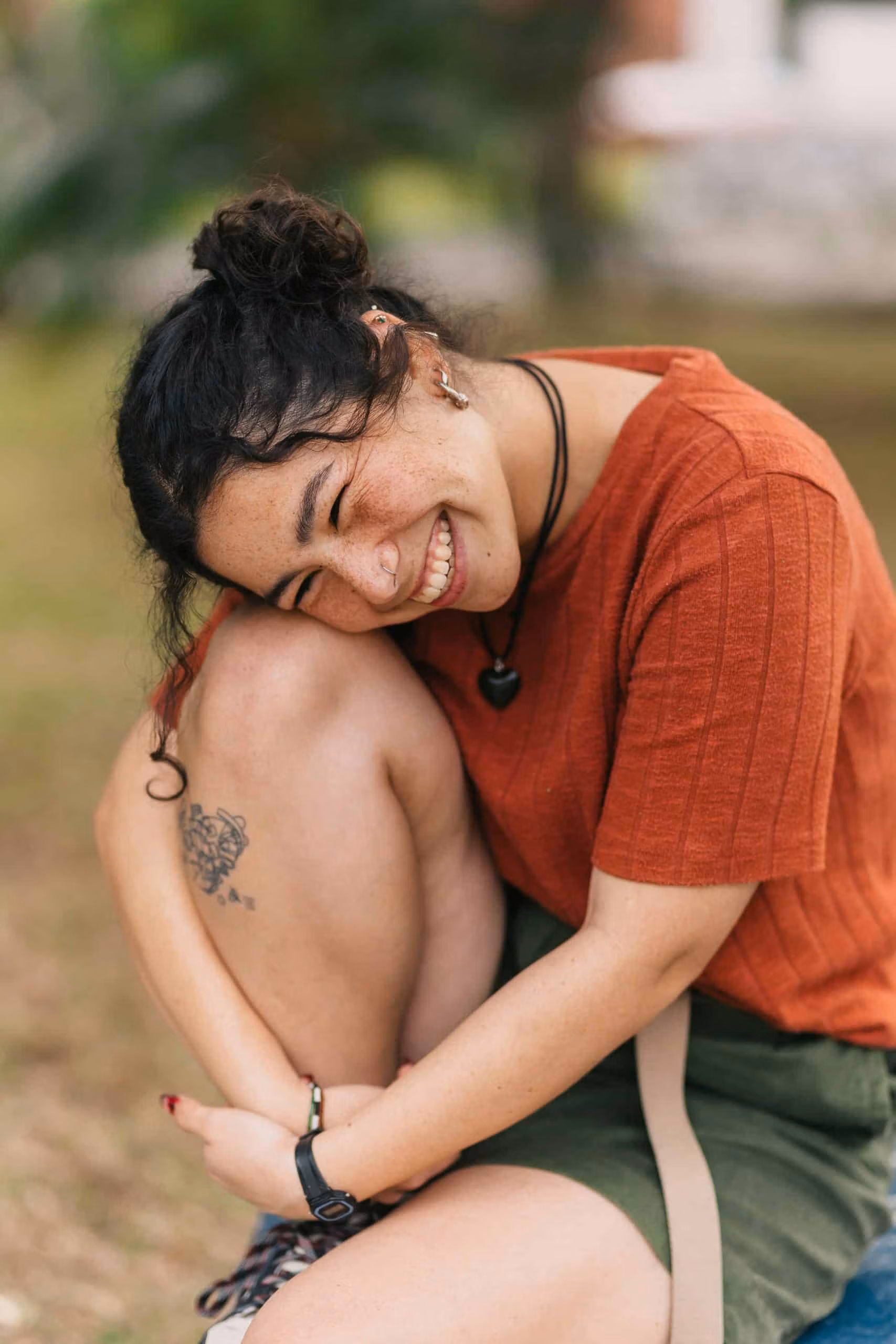 Participant sitting outside on grass, smiling with head resting on knees and arms wrapped around legs.