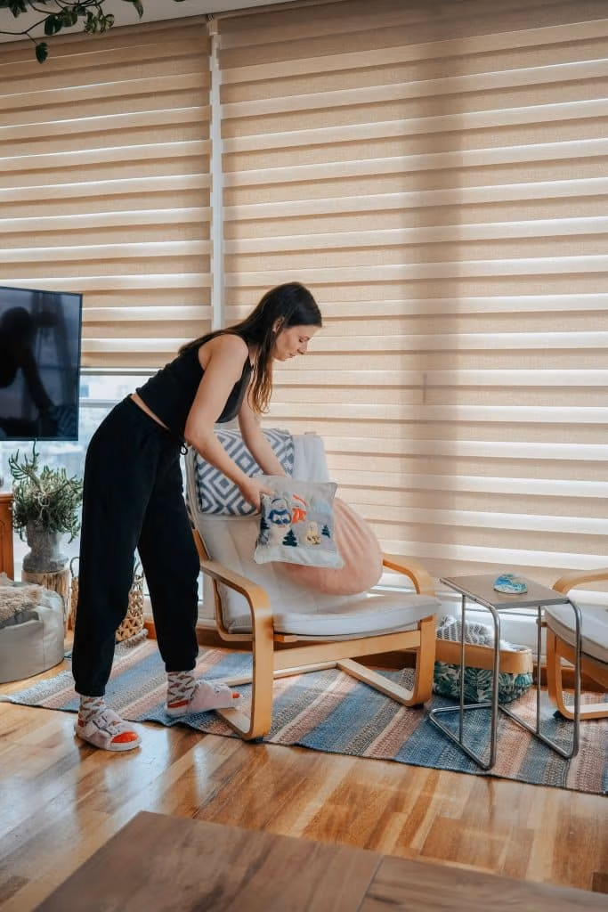 Support worker tidying up a living room by picking up pillows near a chair and indoor plants.